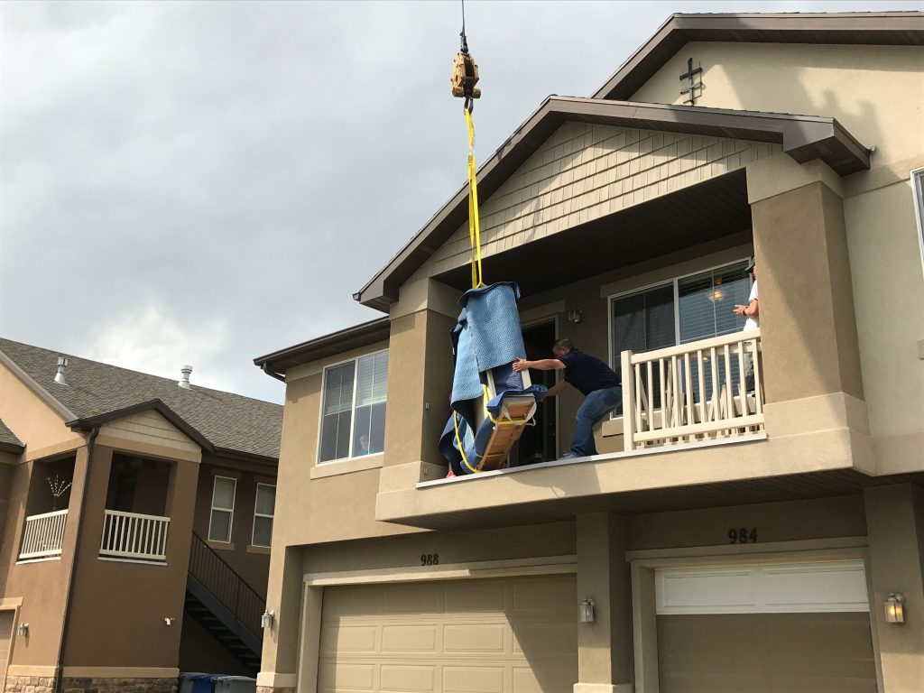 Professional piano movers using crane equipment to move a piano from an upper-floor home in Utah