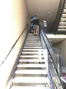 Professional piano movers moving a protected piano up an exterior staircase in Utah